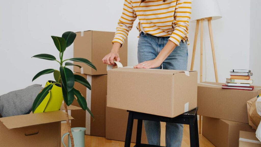 A woman carefully seals a large moving box with packing tape in preparation for a house move. - where to get free moving boxes