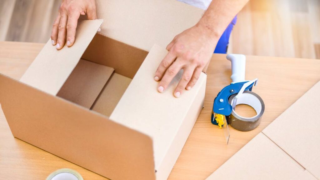 A person prepares a cardboard box for packing, showing the folding of the top flaps before sealing. - where to find free and cheap moving boxes