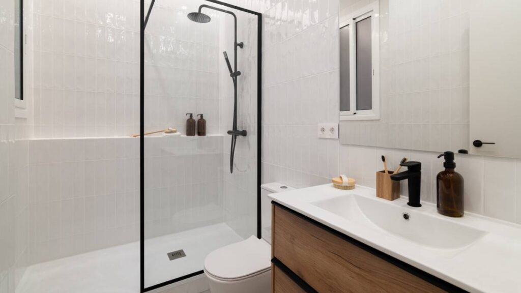 A contemporary, clean bathroom featuring white subway tiles, a black shower frame, and a wooden vanity. - budget bathroom renovation ideas