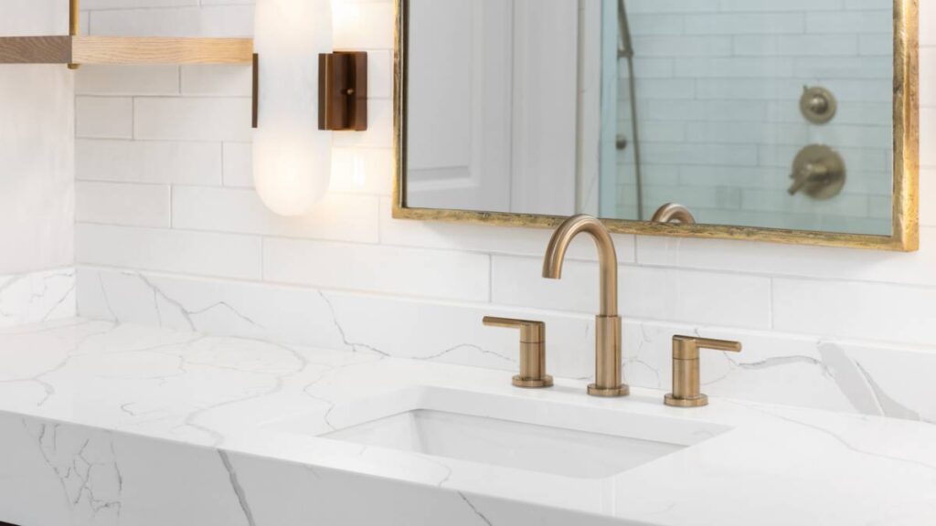 A close-up shot of a bathroom sink featuring a marble-effect countertop and antique brass fixtures. - budget bathroom renovations ideas