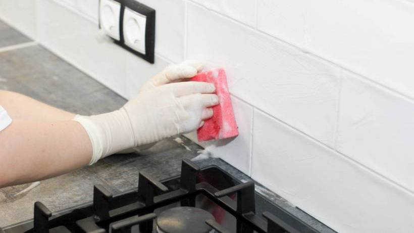 A person wearing white gloves cleans a white tiled kitchen splashback with a pink sponge. - types of kitchen splashbacks