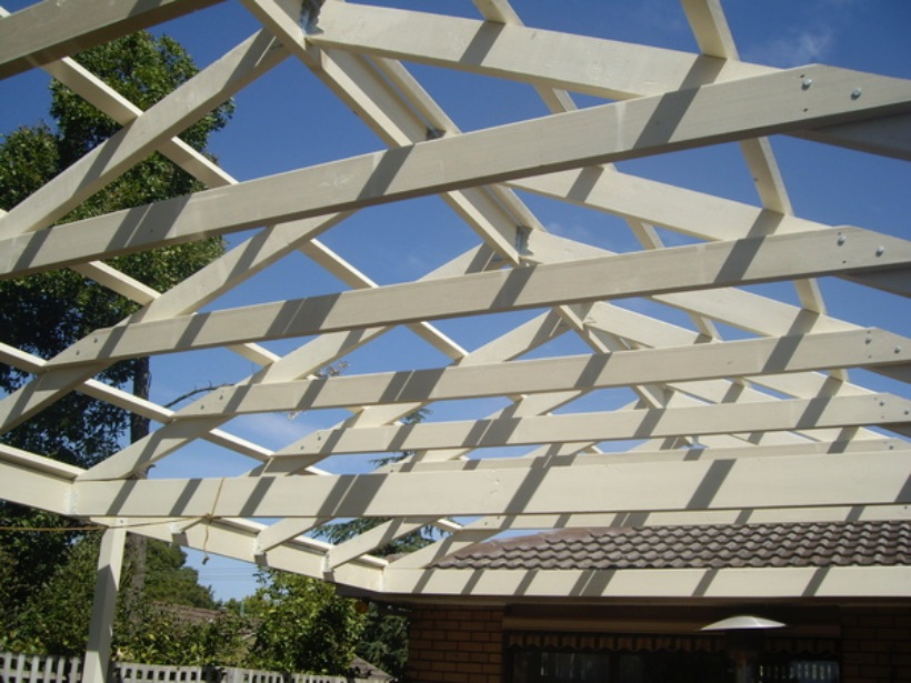 An outdoor carpentry project showcasing the wooden framework of a roof under a clear blue sky.