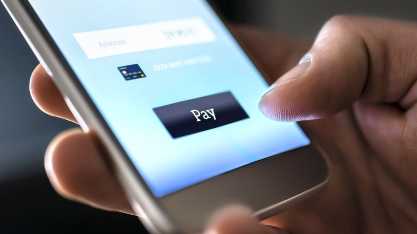 A close-up of a hand pressing the 'Pay' button on a smartphone screen to complete an online payment.